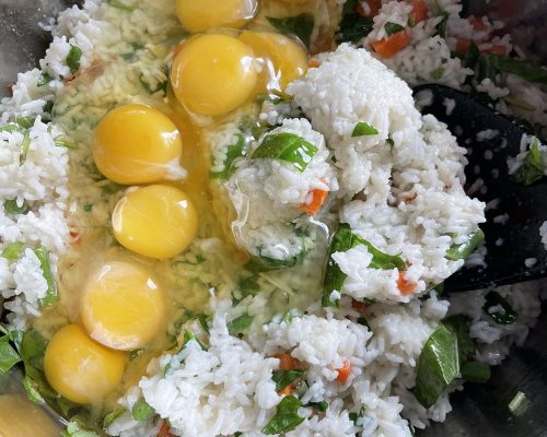 A mixing bowl of eggs, rice, greens, and carrots