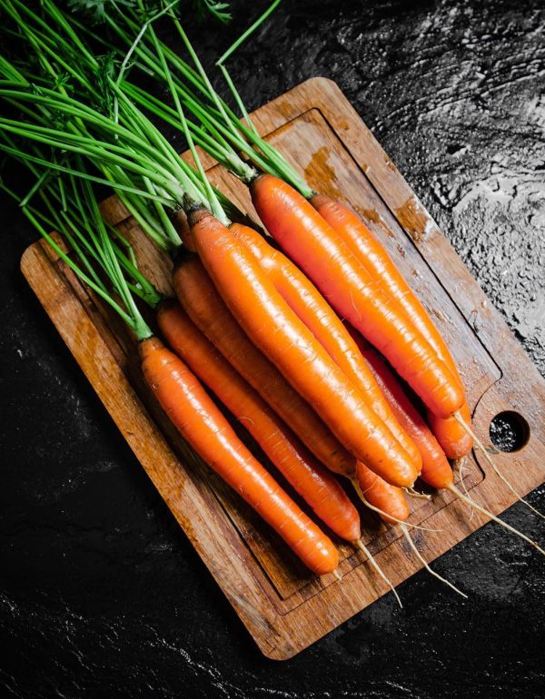 Fresh organic carrots on a wood cutting board on a black table.