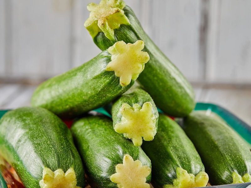 Stacked fresh zucchini on a plate on a gray wooden background.